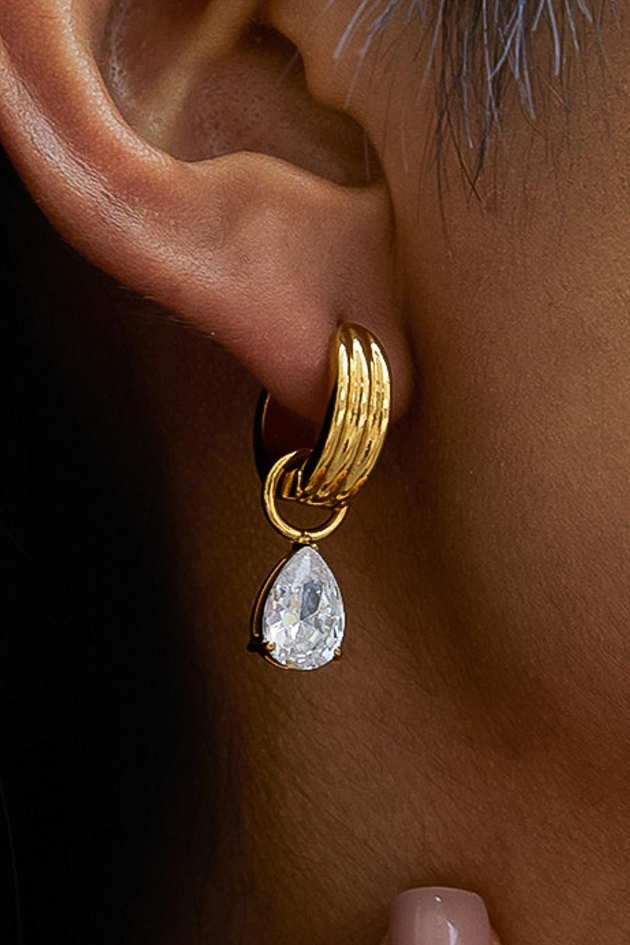 Gold hoop earring with a teardrop-shaped gemstone worn on an ear.