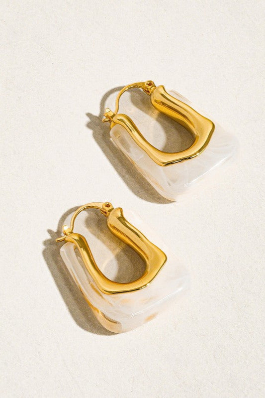 Gold hoop earrings with a white stone on a beige background