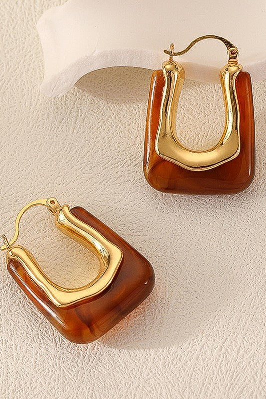 Gold and brown hoop earrings on a textured beige surface