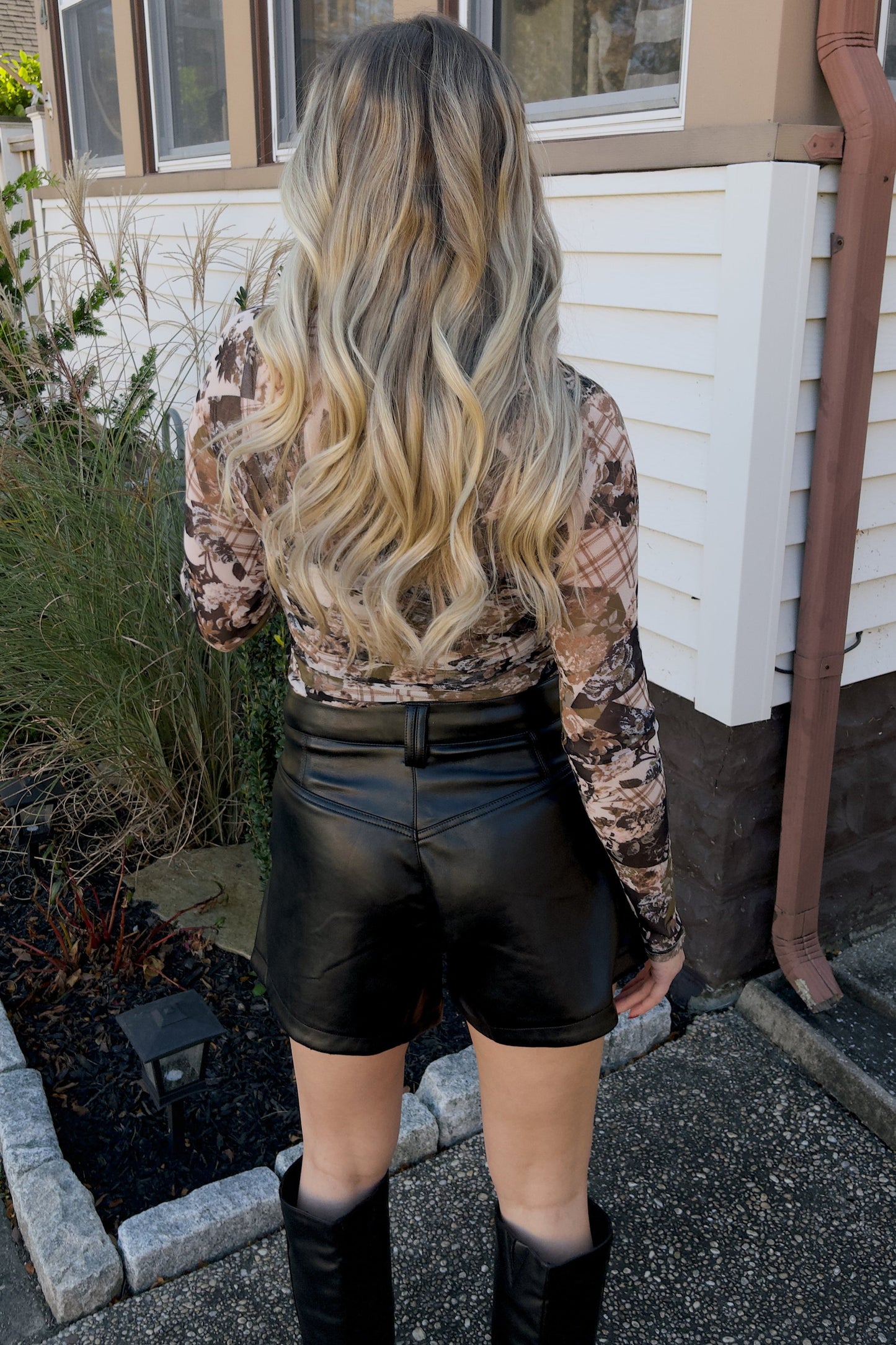 A person wearing black leather shorts and a floral print top, standing outdoors.