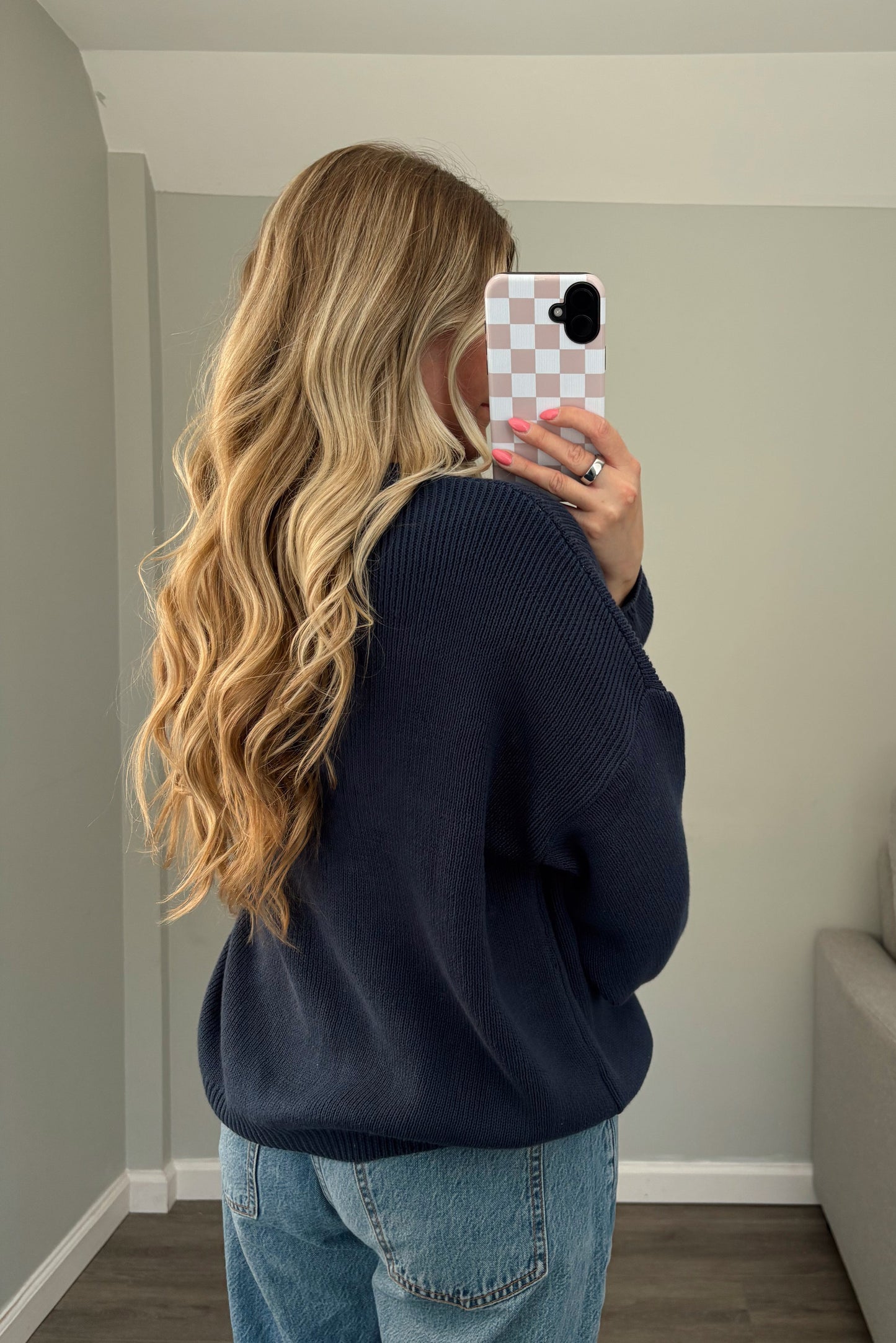 Person wearing a navy sweater and blue jeans taking a mirror selfie.