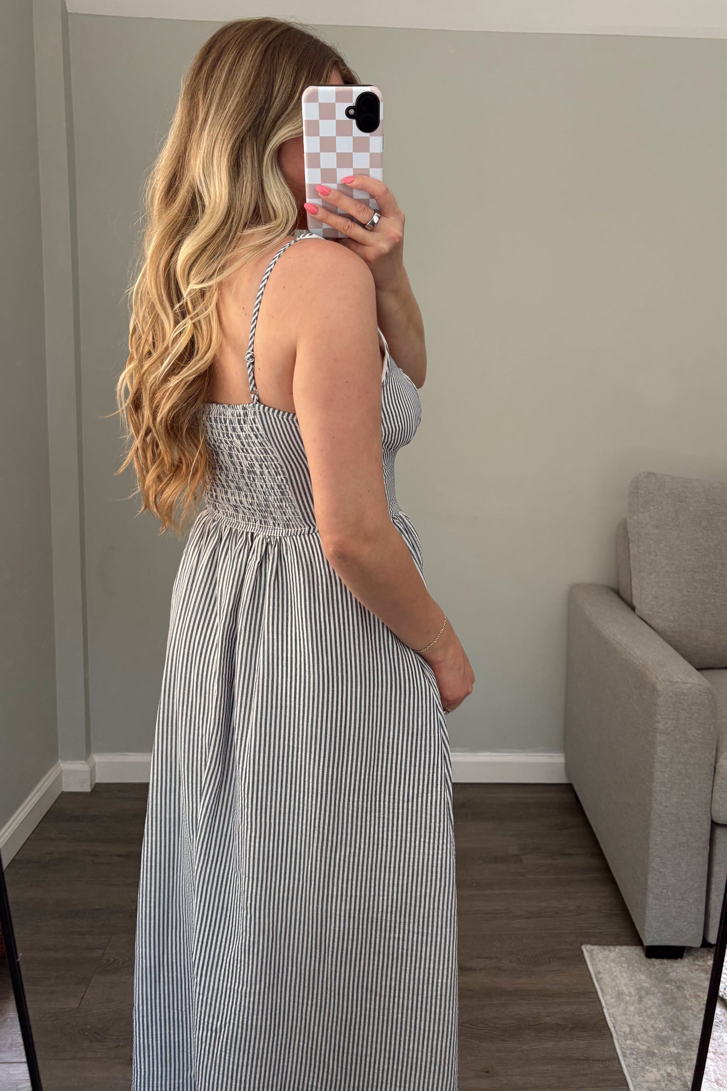 Woman taking a mirror selfie wearing a gray striped dress in a room with a couch and rug.