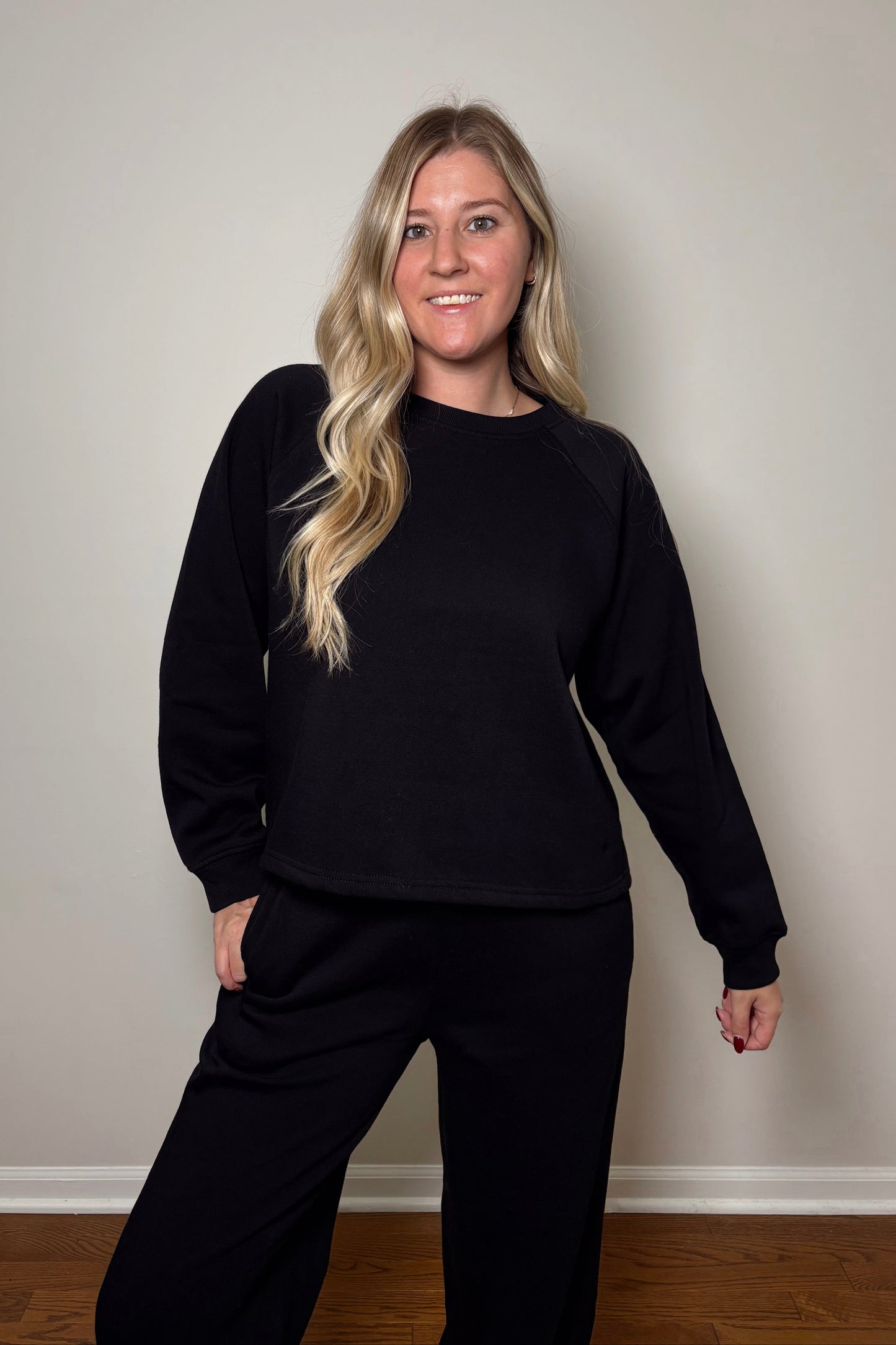 Woman wearing a black sweat set standing against a plain wall.