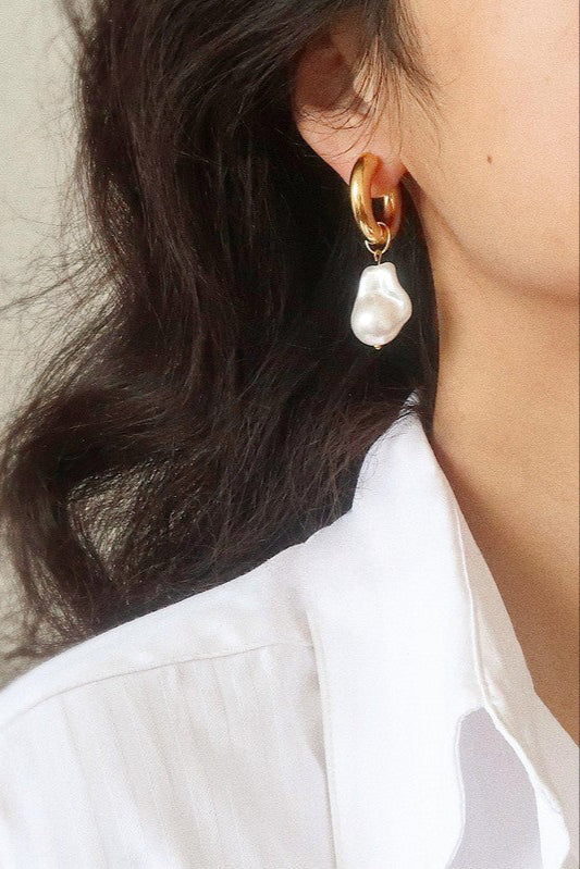 Oceana gold-tone hoop earring with an irregular white faux pearl drop, worn beside dark hair and a white collared shirt.

