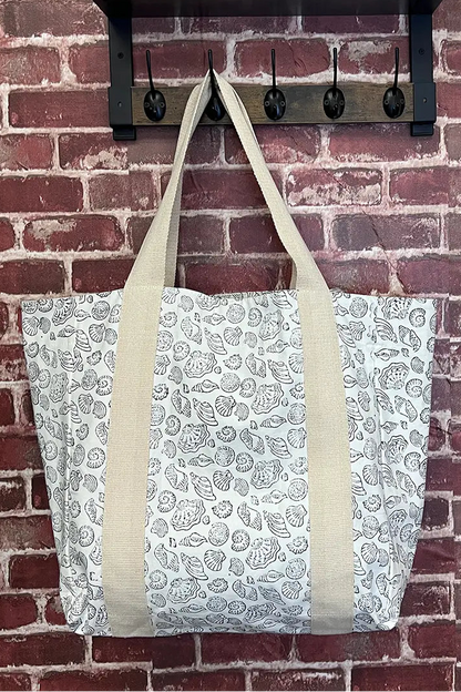 Tote bag with seashell pattern hanging on a brick wall with hooks.