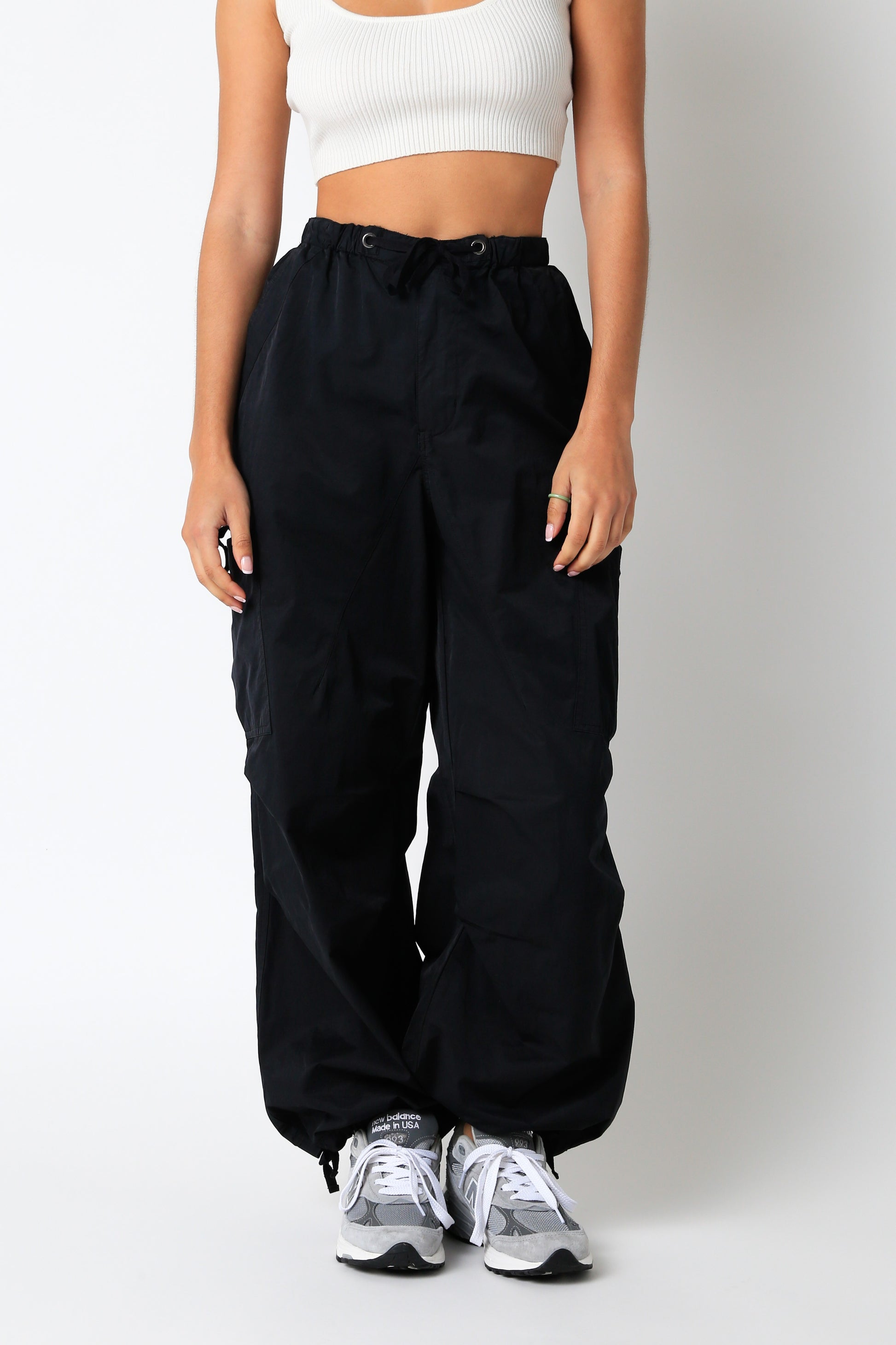 Person wearing black high-waisted pants and white sneakers on a plain background