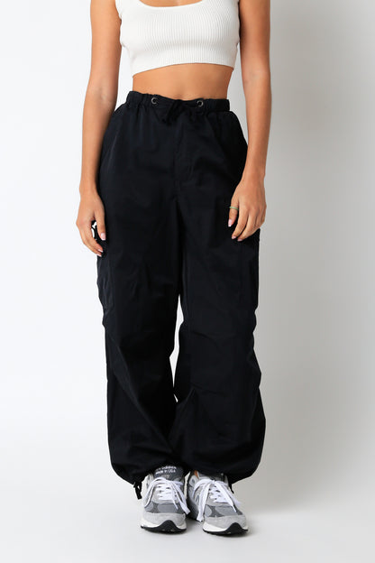 Person wearing black high-waisted pants and white sneakers on a plain background