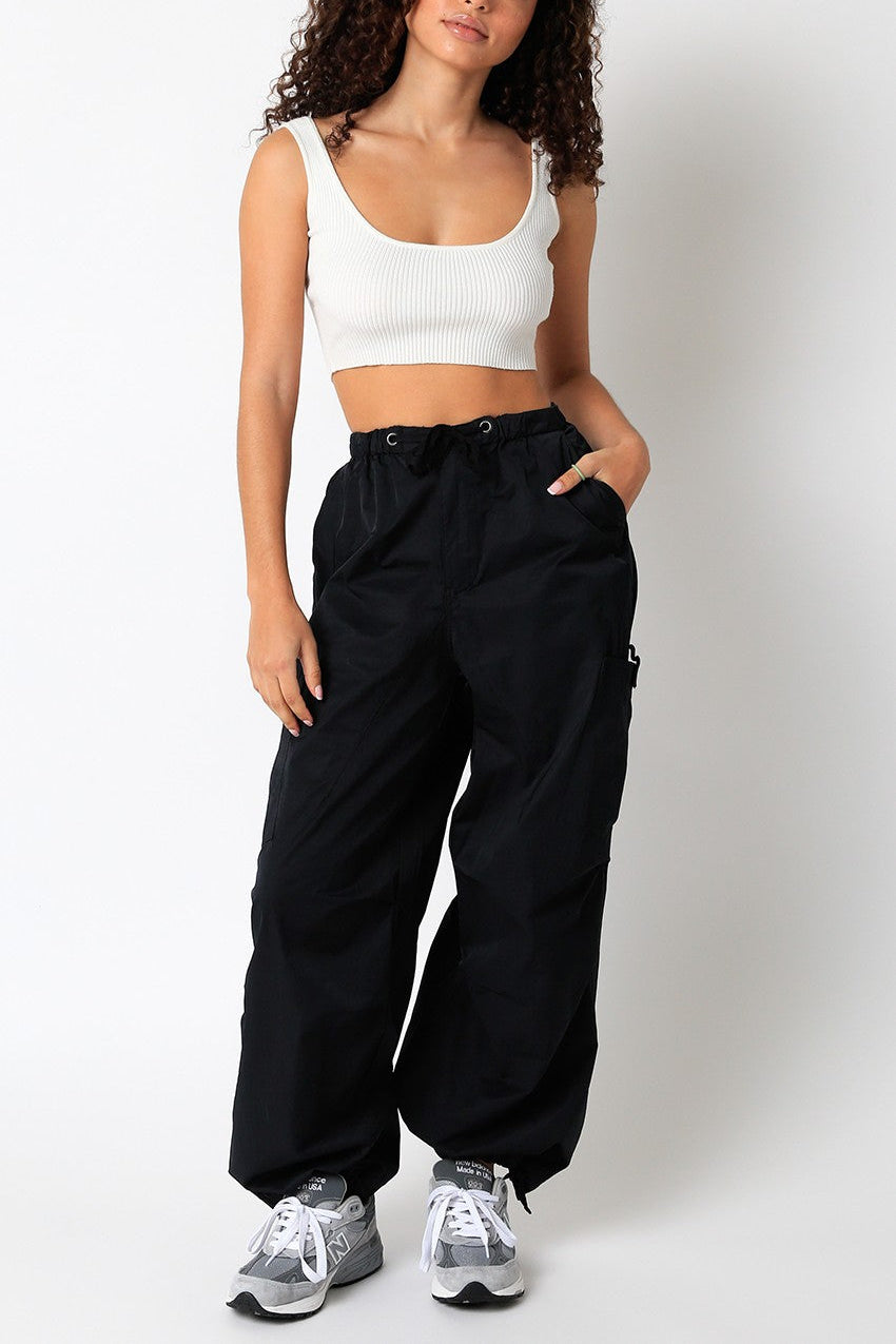 Woman wearing a white tank top and black high-waisted pants on a plain background