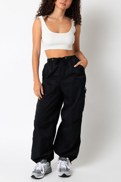 Woman wearing a white tank top and black high-waisted pants on a plain background