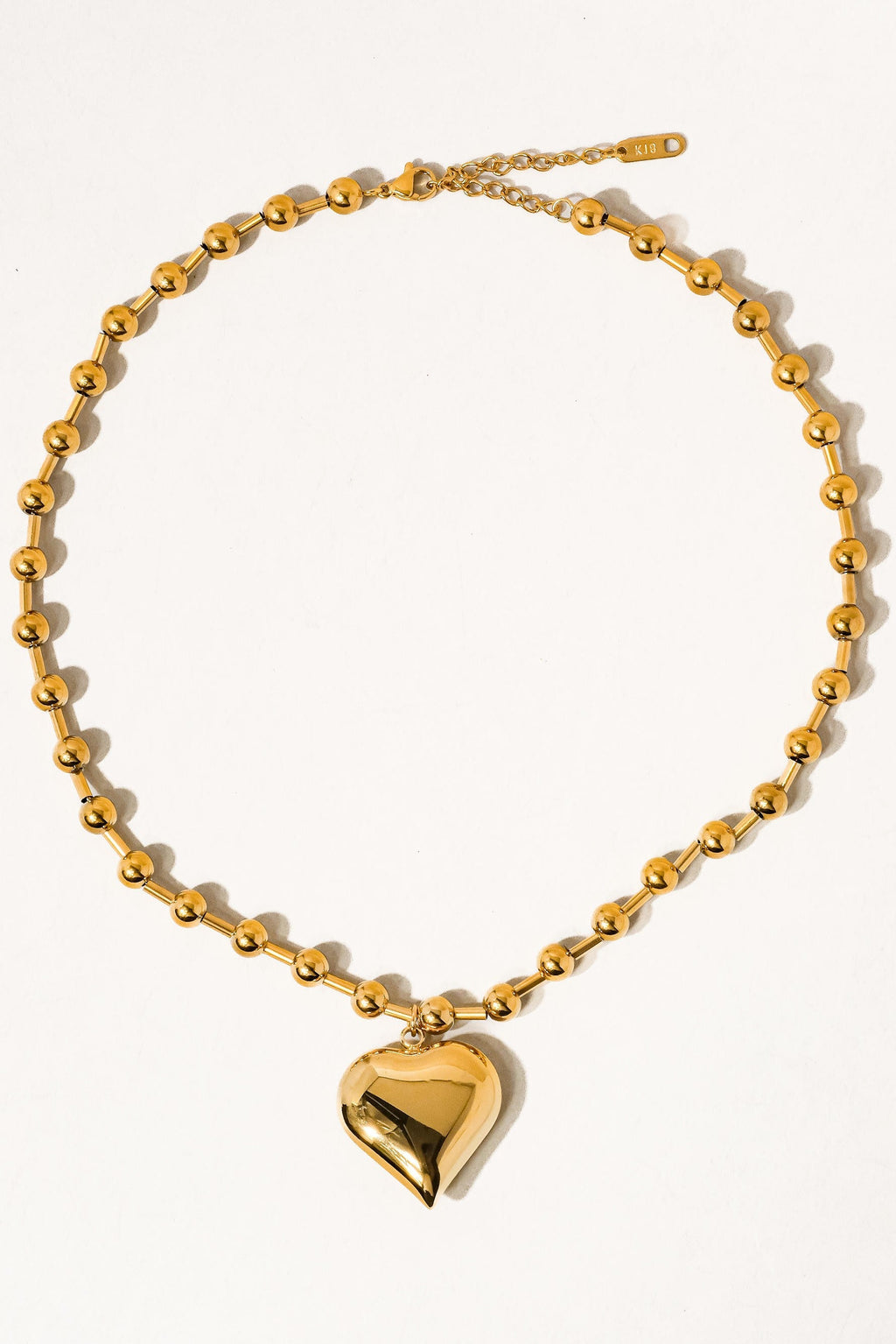 Paris gold-tone heart pendant necklace laid flat on a cream background, showing its beaded chain, clasp, and extension.

