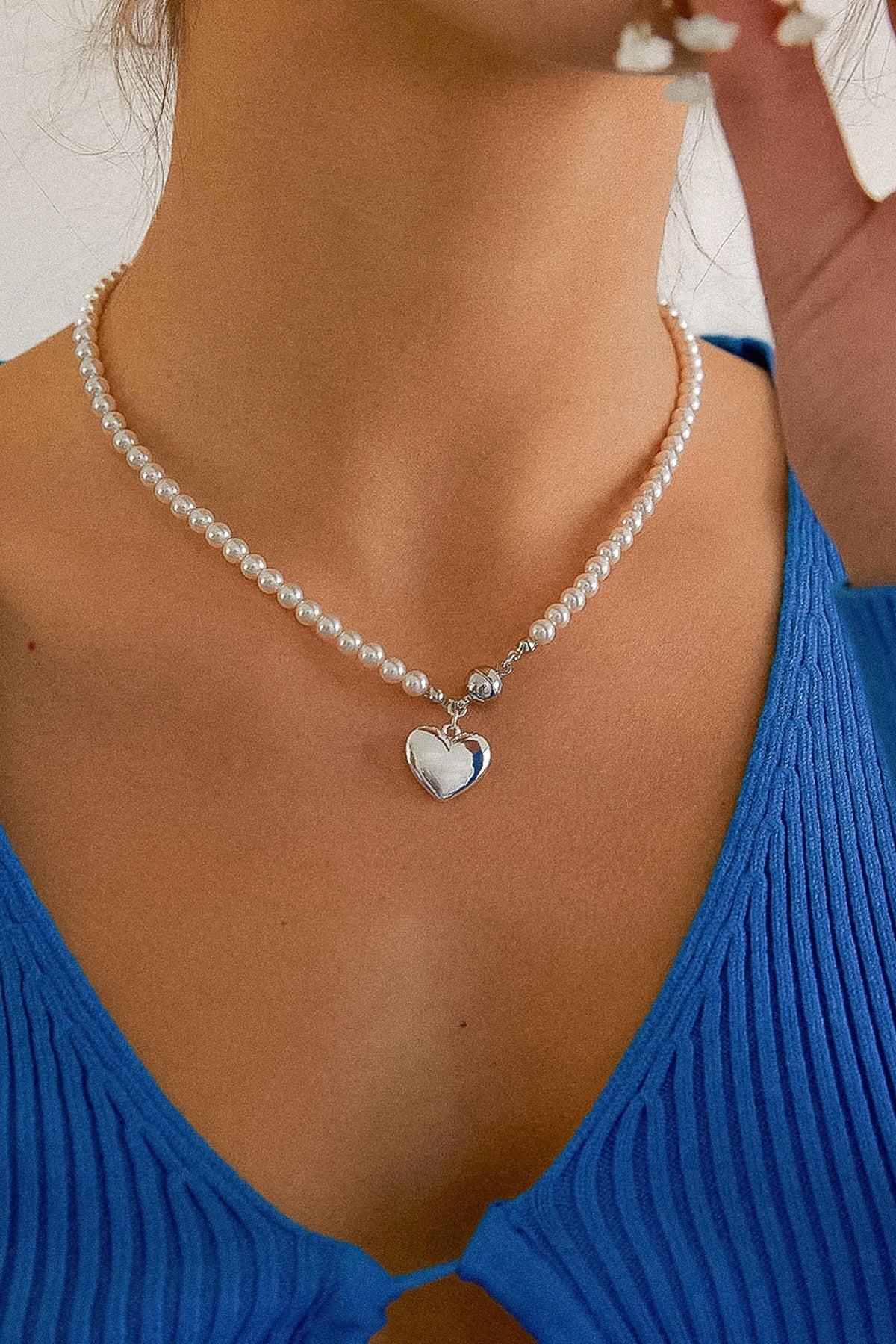 Gemma pearl-style beaded necklace with a silver-tone heart pendant worn with a blue ribbed top.

