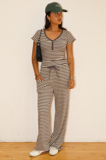 woman wearing a striped henley tee and matching drawstring pants against a white wall. 