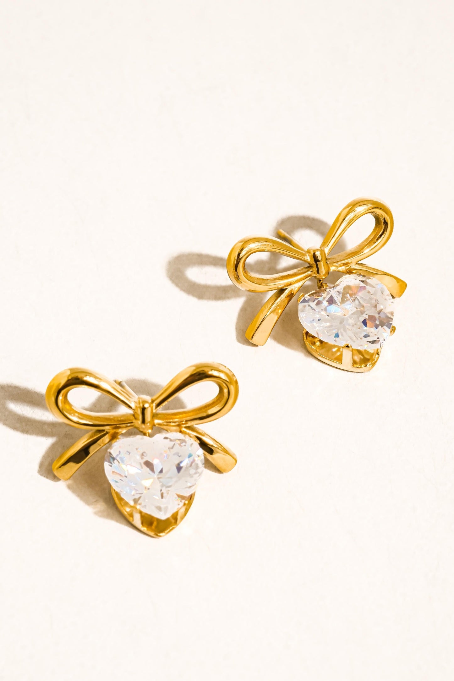 Gold bow-shaped earrings with clear gemstones on a white background