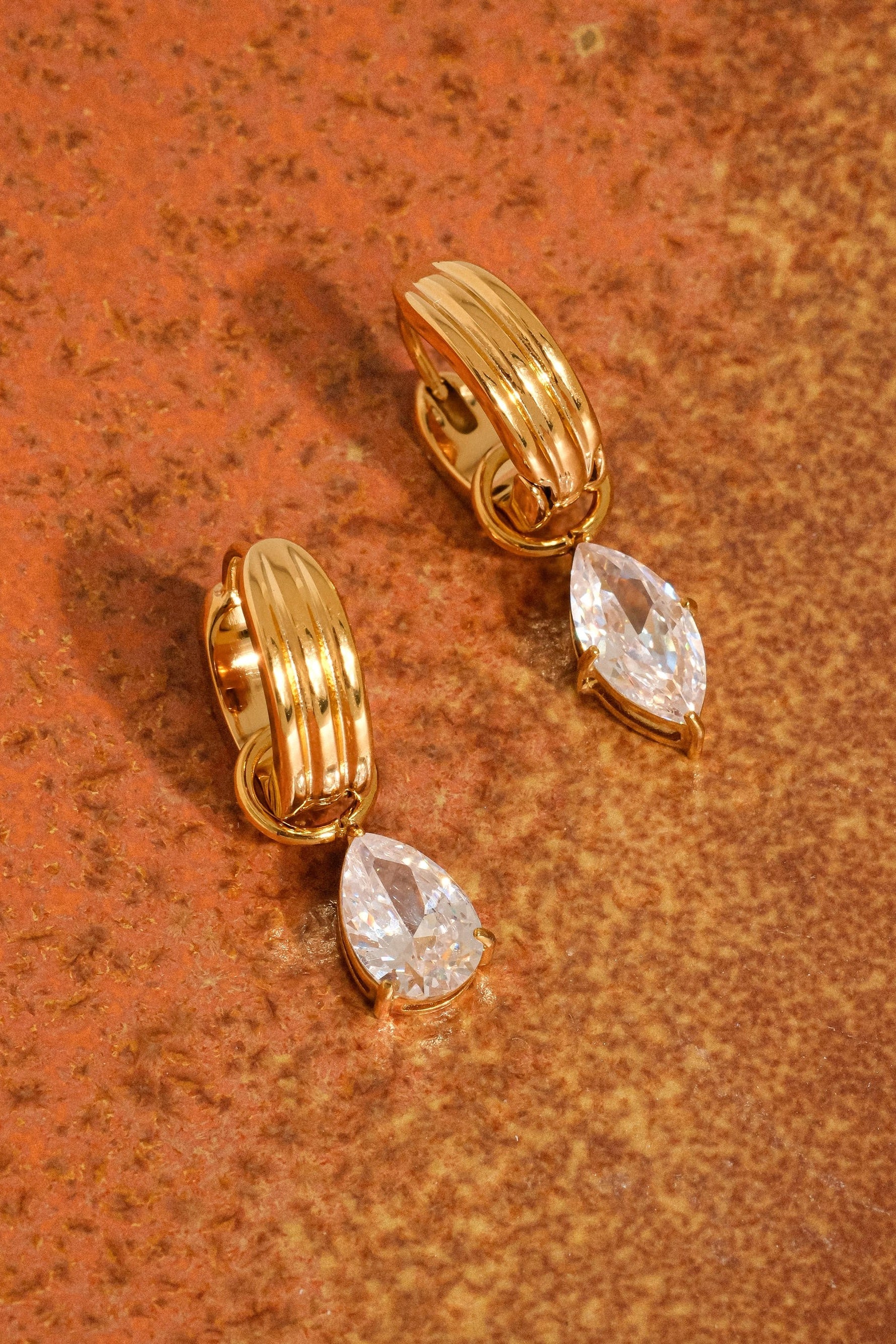 Gold hoop earrings with teardrop-shaped gemstones on a brown surface