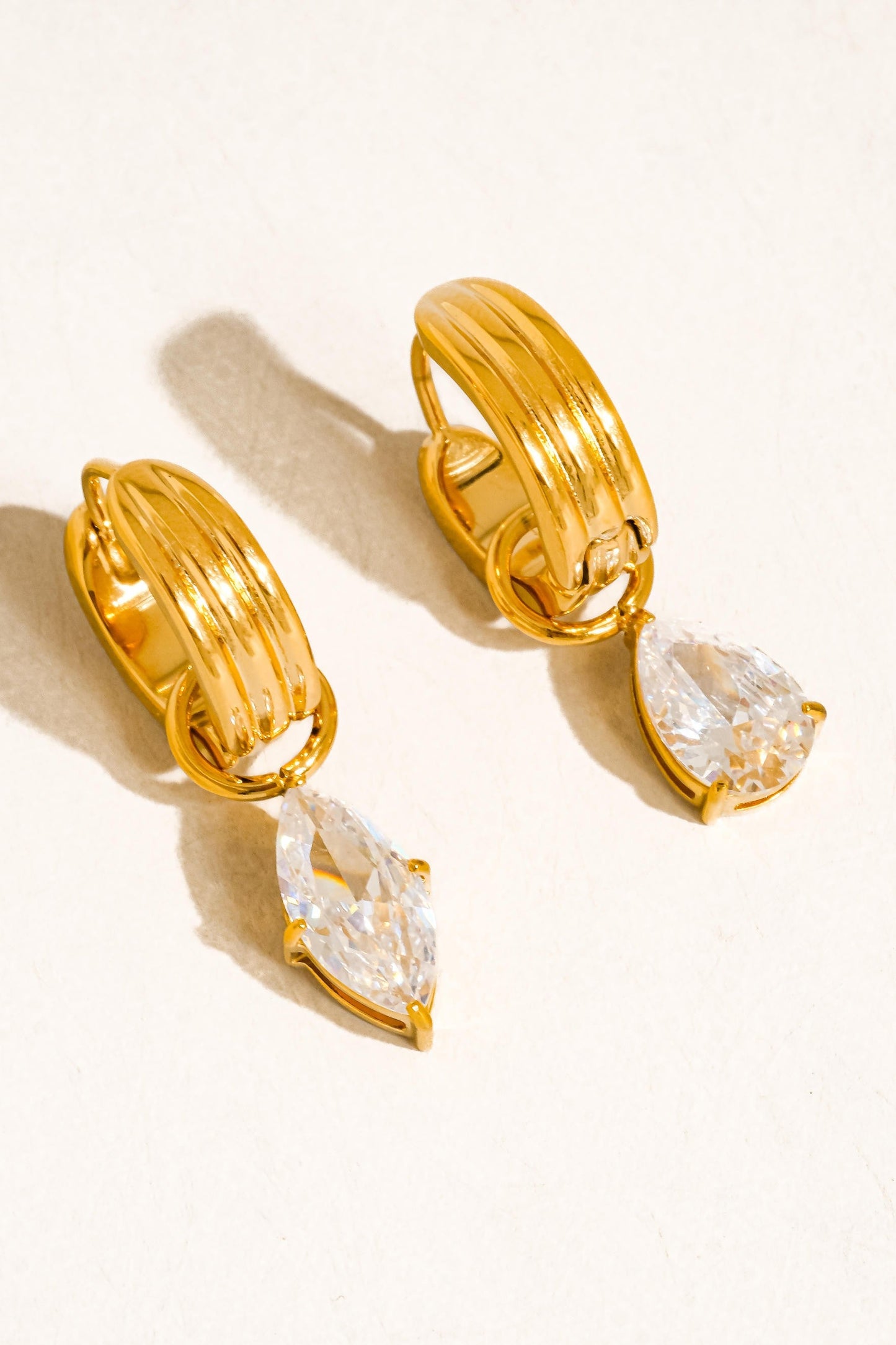 Gold hoop earrings with teardrop-shaped clear stones on a white background