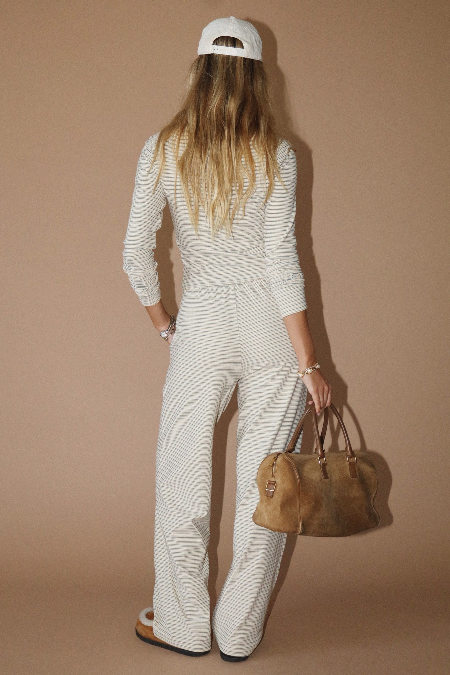 Person wearing a white outfit with a brown bag against a beige background