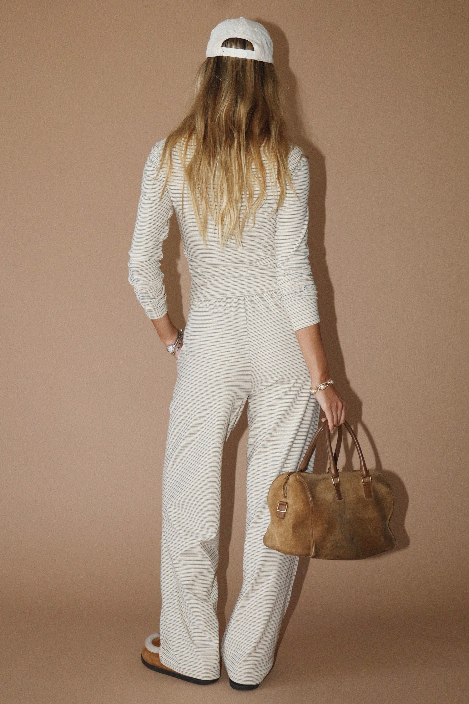Person wearing a white outfit with a brown bag against a beige background