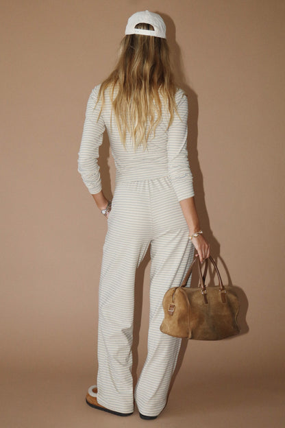 Person wearing a white outfit with a brown bag against a beige background