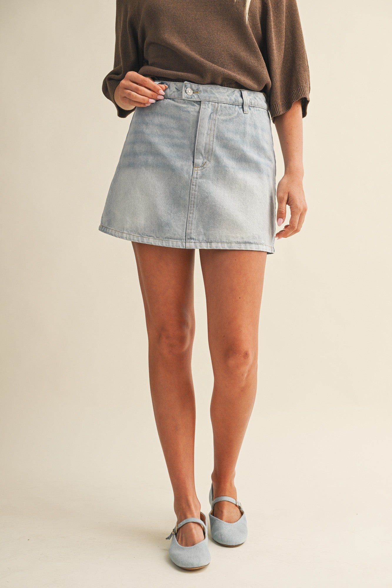 Person wearing a light blue denim skirt on a plain background
