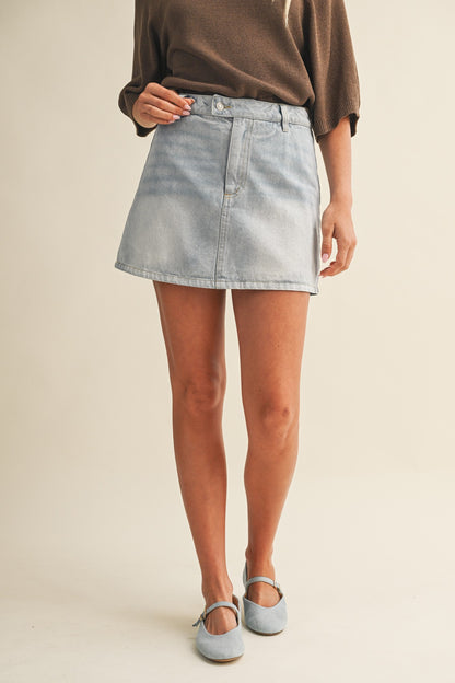 Person wearing a light blue denim skirt on a plain background