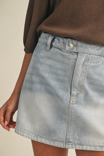 Light blue denim skirt worn with a brown sweater on a neutral background