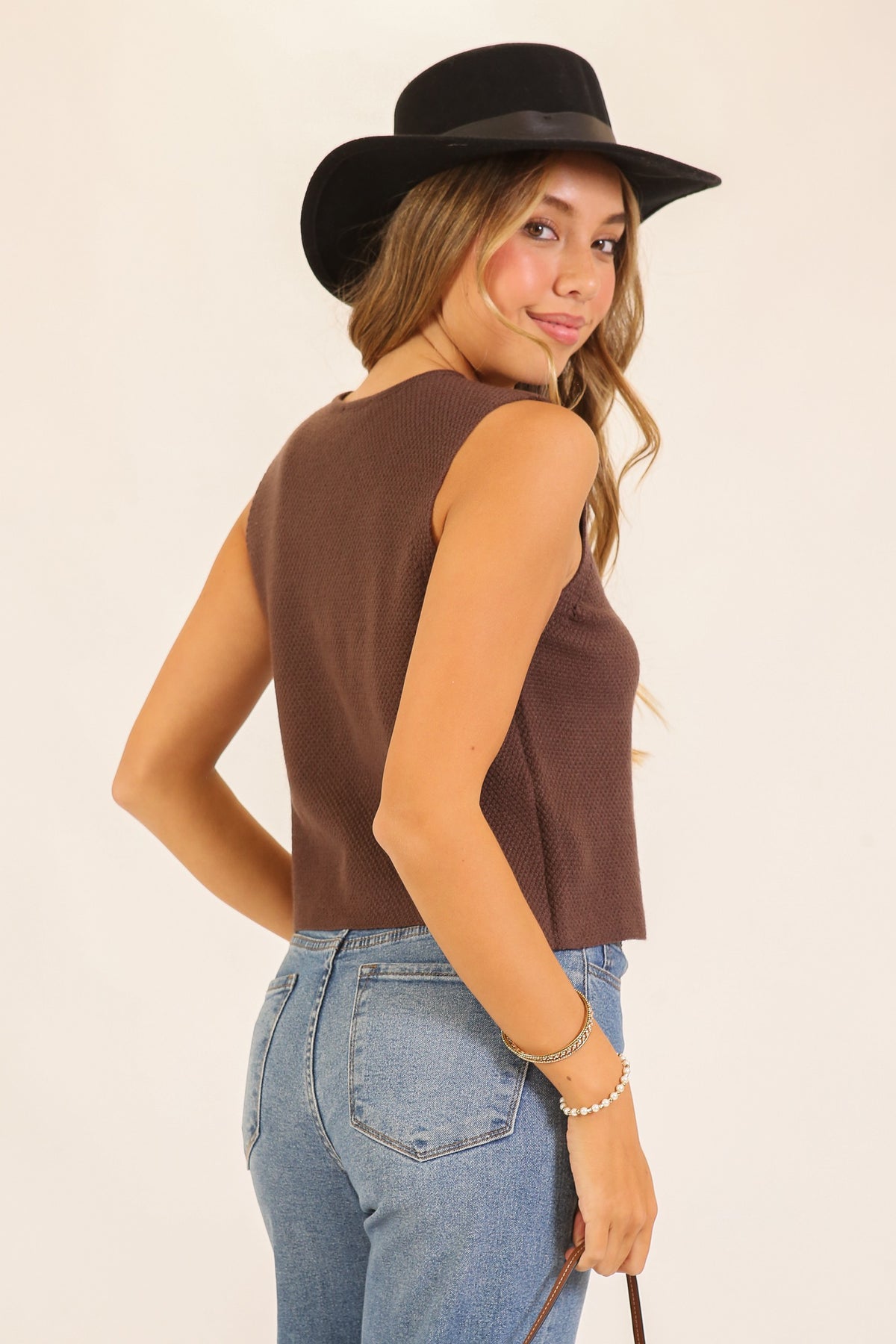 Woman wearing a brown sleeveless top and black hat on a beige background