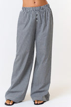 Front view of black-and-white gingham wide-leg pants showing the faux button detail and full-length hems over black sandals.

