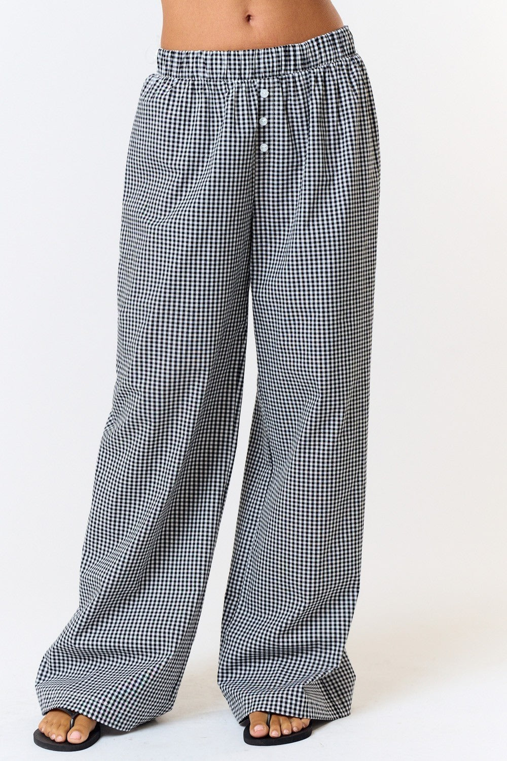 Front view of black-and-white gingham wide-leg pants showing the faux button detail and full-length hems over black sandals.

