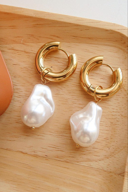 Pair of Oceana polished gold-tone hoops with irregular white faux pearl drops resting on a wooden tray.

