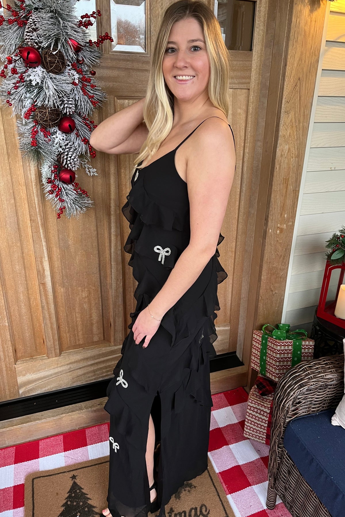 Side view of the Mia black maxi dress showing its side slit, layered ruffles, and rhinestone bow details.

