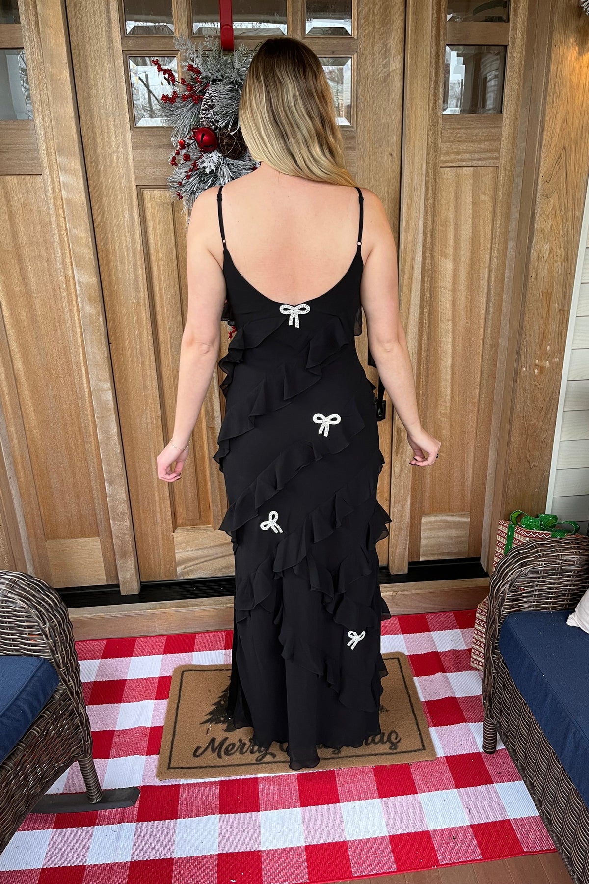 Back view of the Mia black ruffle maxi dress showing its low scoop back, adjustable straps, and rhinestone bows.


