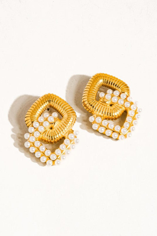 Pair of Cometa chain-link earrings with textured gold-tone links and white faux pearl accents on a cream background.

