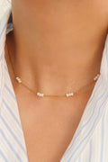 Leilani gold-tone chain choker with small white freshwater pearl clusters, worn with a light blue striped shirt.

