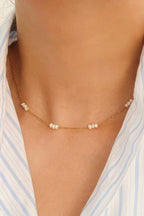 Leilani gold-tone chain choker with small white freshwater pearl clusters, worn with a light blue striped shirt.

