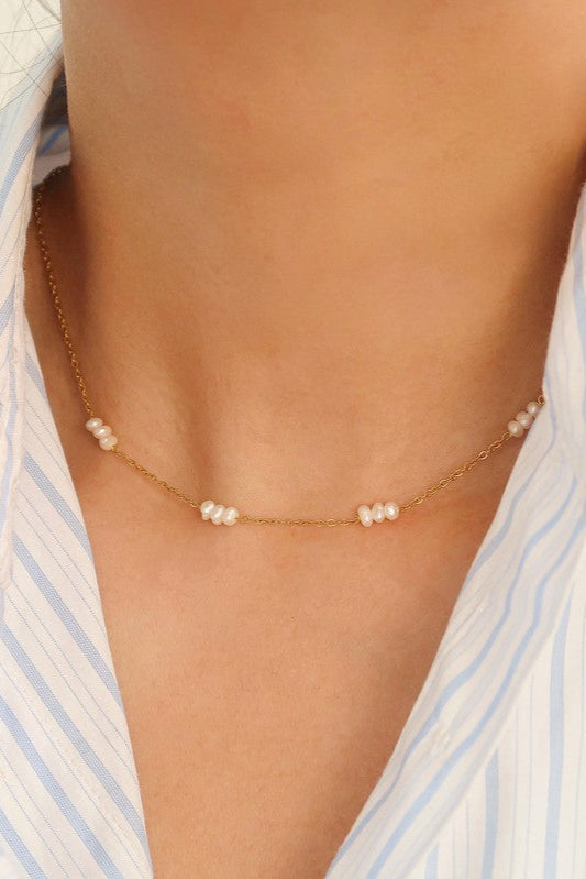 Leilani gold-tone chain choker with small white freshwater pearl clusters, worn with a light blue striped shirt.


