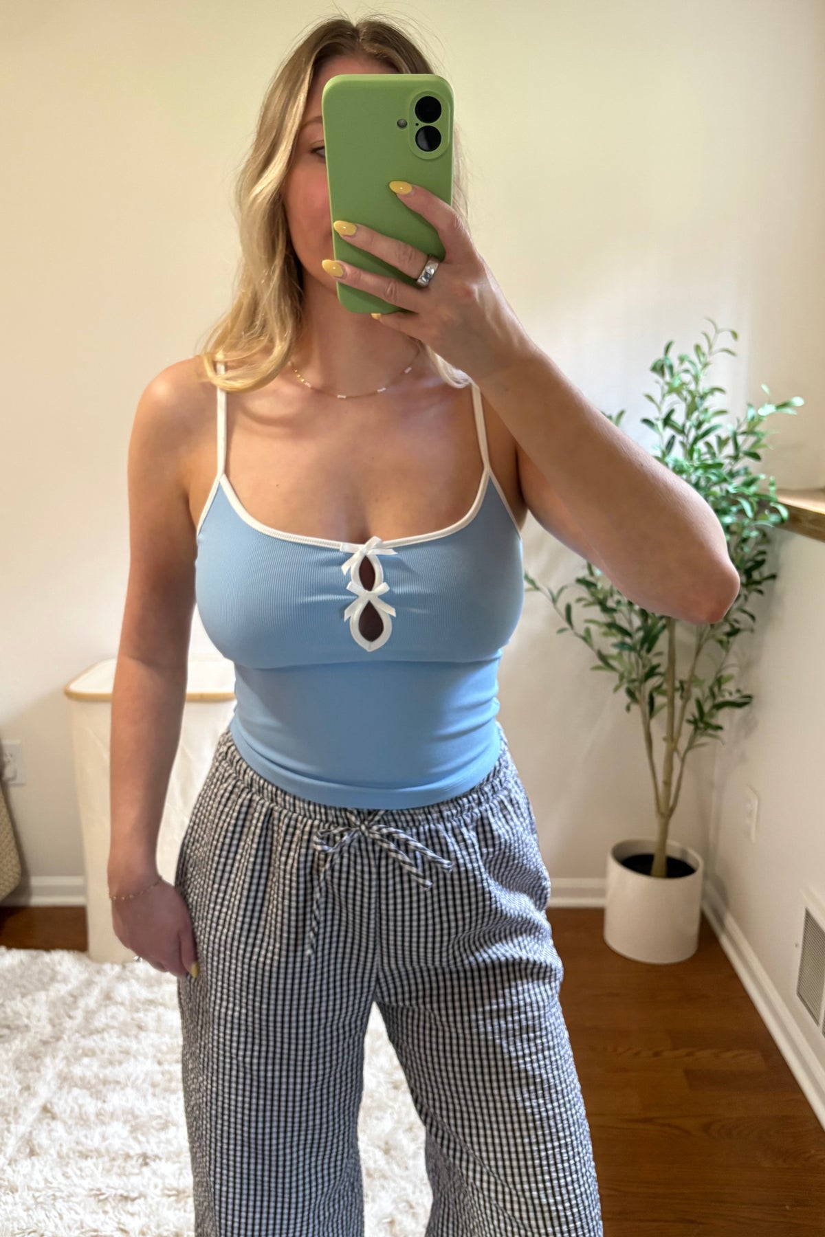 Mirror selfie showing the Elsie light blue cropped tank with white trim and two bow-accented front cutouts, paired with gingham pants.

