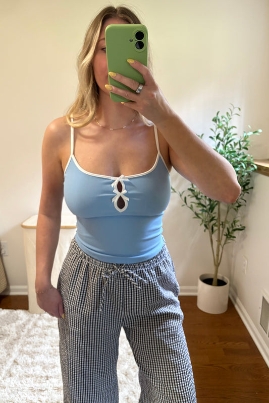 A person wearing a blue tank top with white bow detail and white and black checkered pants.