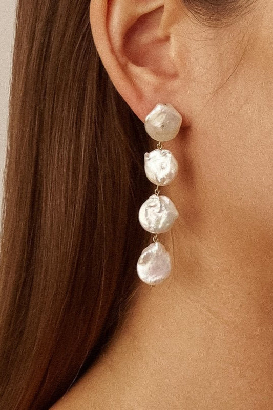 Heloise faux pearl drop earring worn beside brown hair, showing four irregular white discs connected by small gold-tone links.


