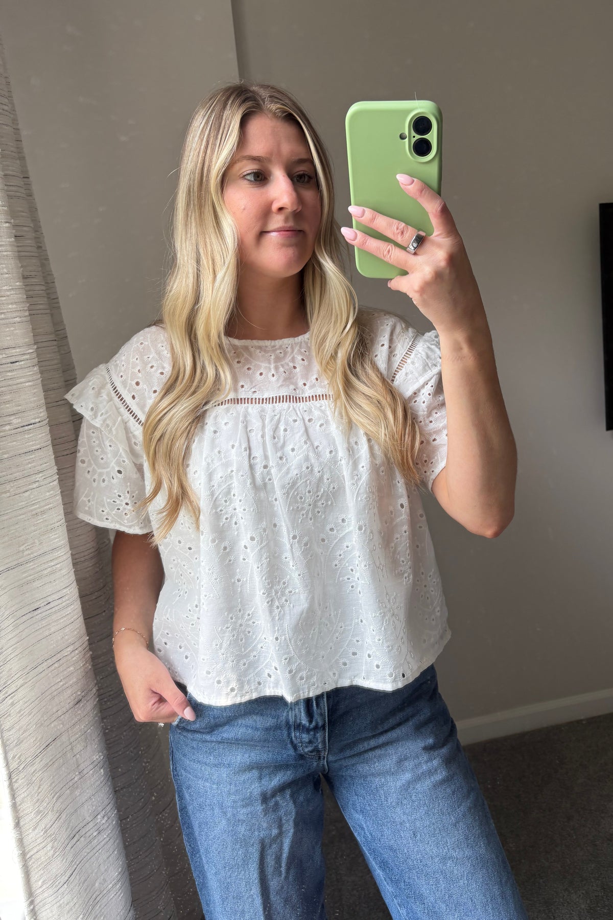 Blossom white cotton eyelet blouse worn untucked with blue jeans, showing the gathered front and short ruffle sleeves.

