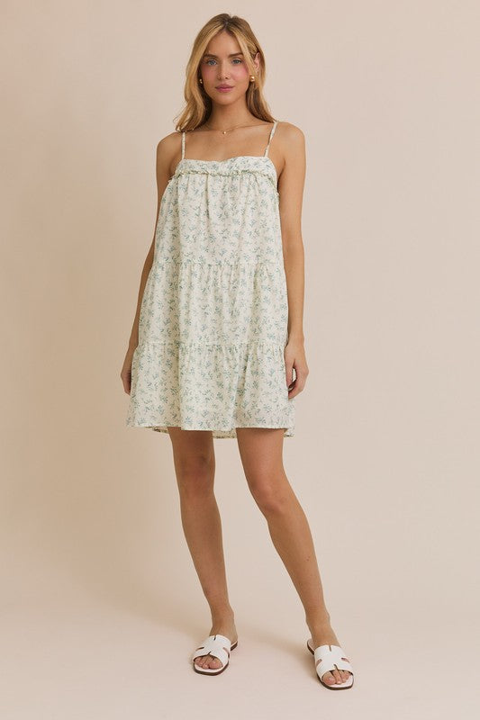 Full-length front view of the Meadow Muse floral mini dress styled with white slide sandals against a beige background.

