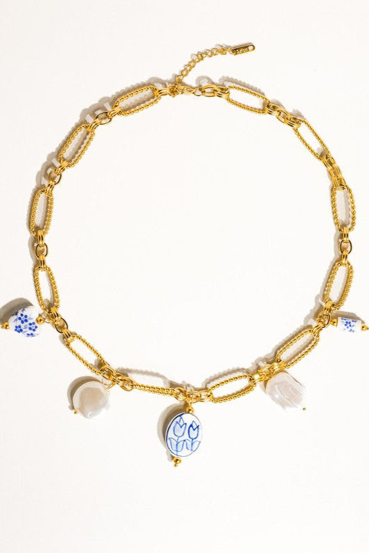 Riela floral charm necklace laid flat on a cream background, showing textured oval links, dangling charms, and an extension chain.

