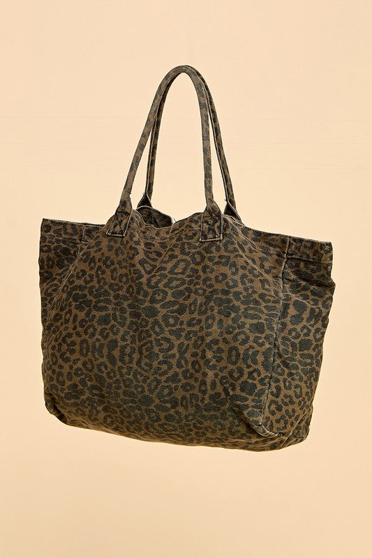 Angled view of the Cheetah Girls animal print tote bag showing long shoulder handles, dark spotted fabric, and a wide side panel against a peach background.

