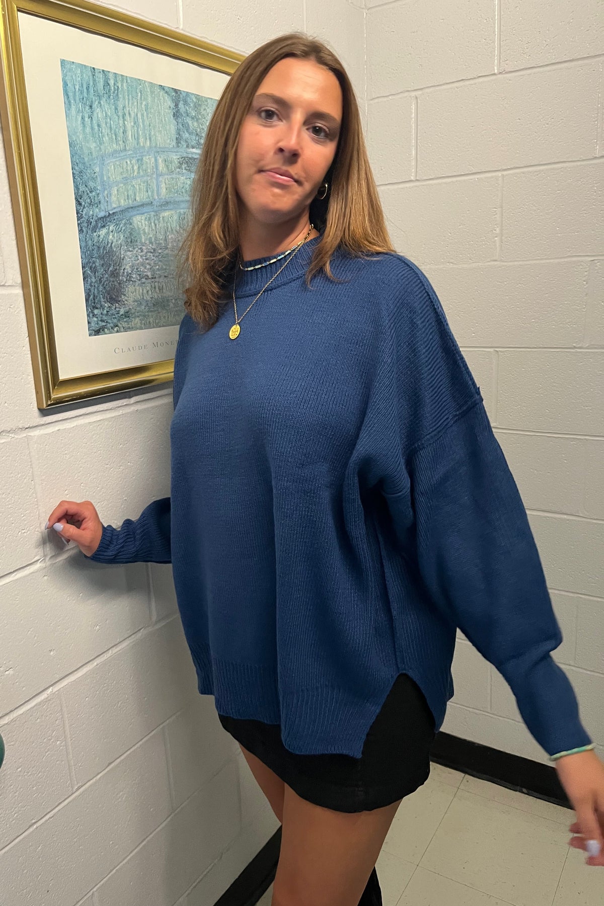 Model extending one arm to show the roomy sleeve and side slit of a blue oversized sweater.

