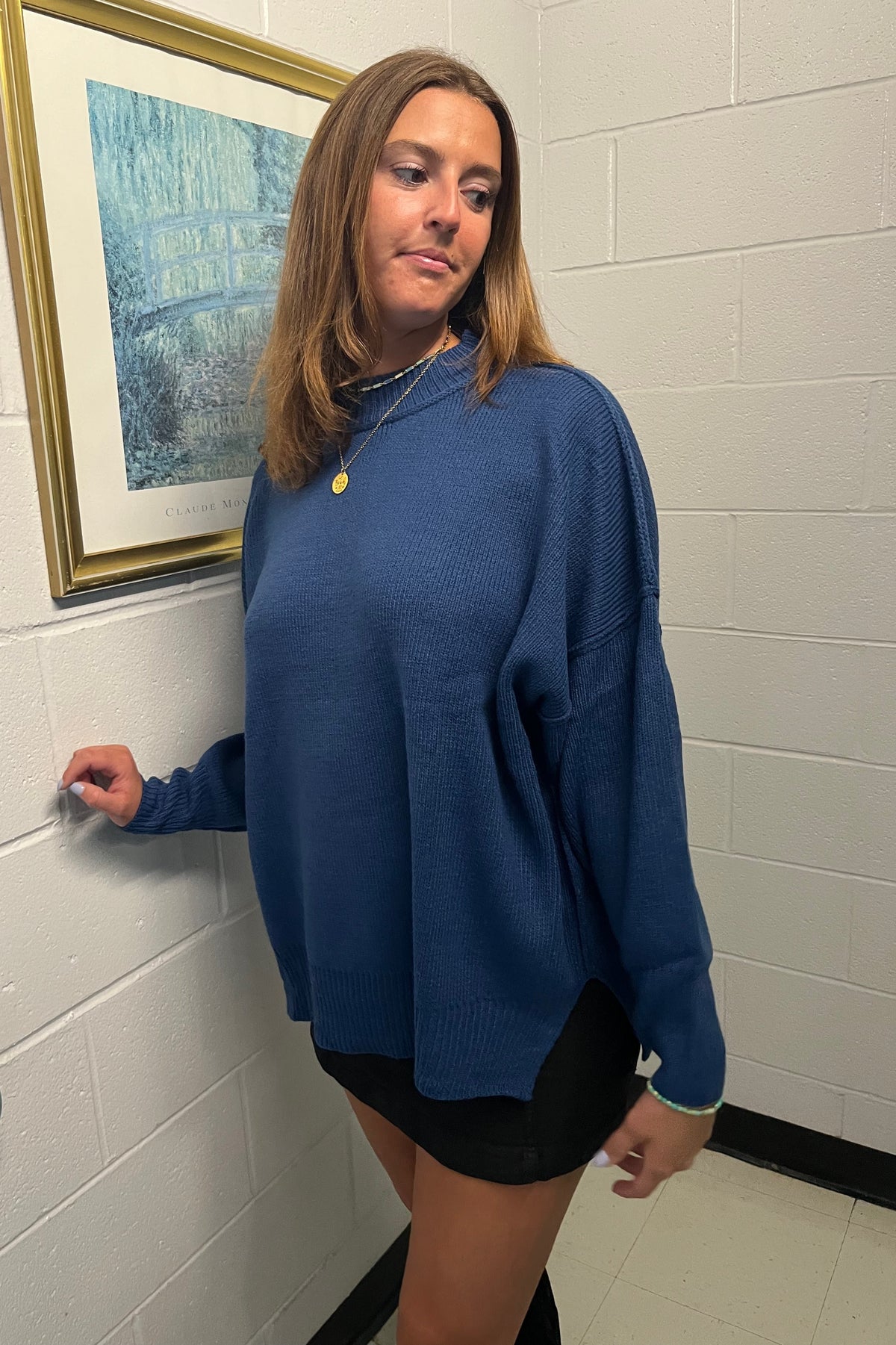 Model wearing a blue oversized knit sweater with dropped shoulders and long sleeves, paired with a black mini skirt.

