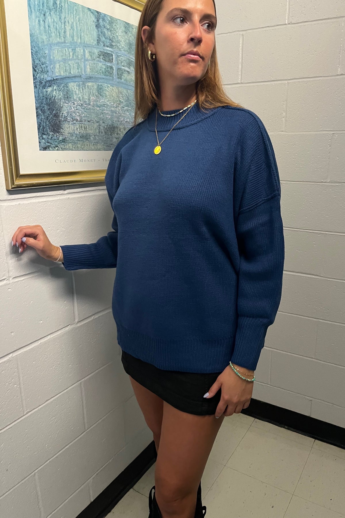 Front view of the Jordyn blue knit sweater showing its high crew neckline, exposed shoulder seams, and ribbed cuffs.

