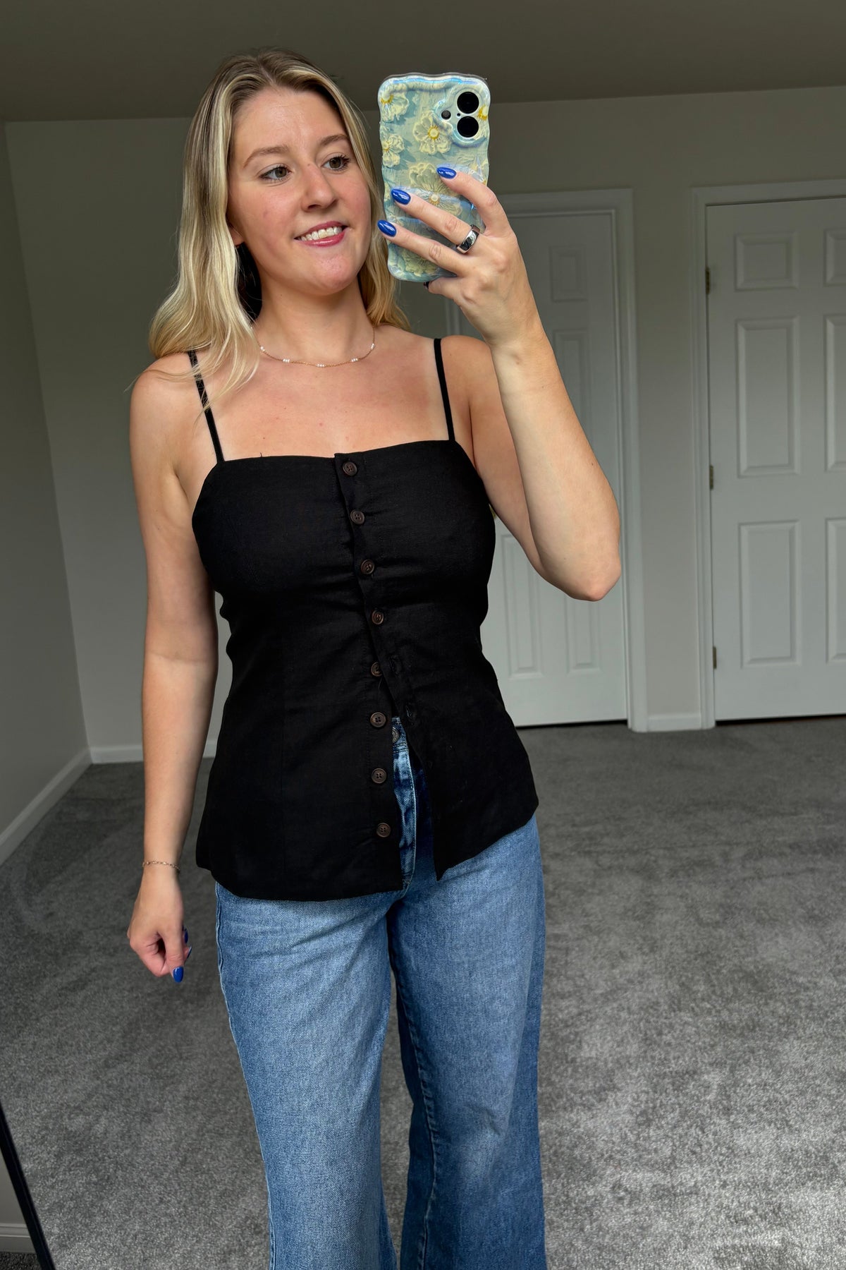 Spencer black button-front top worn with blue jeans, showing its square neckline, thin adjustable straps, and tailored waist.


