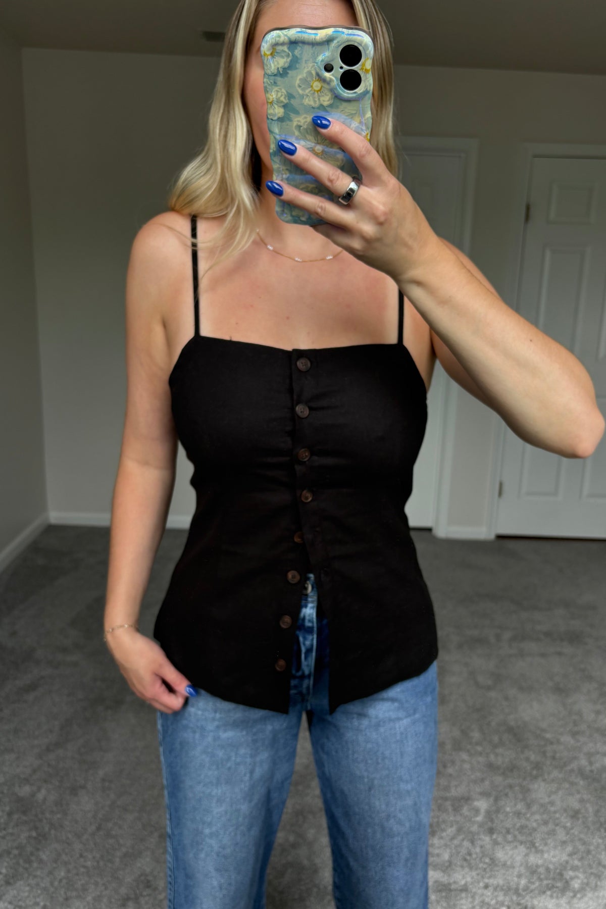 Closer front mirror view of the Spencer black top showing the button closure and lower buttons worn open over blue jeans.

