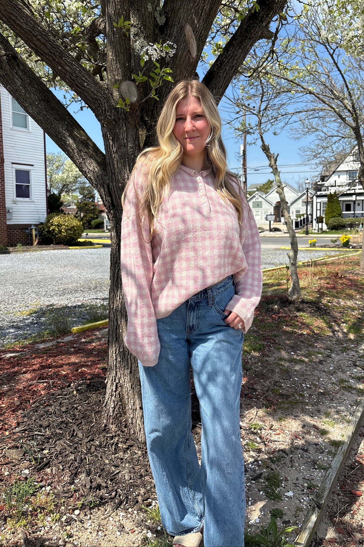 Woman wearing the Rosé pink gingham knit sweater with wide-leg jeans beside a tree