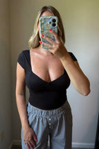 Close front mirror view of the Lark black top showing its sweetheart neckline, fitted shape, and cropped hem above gingham pants.

