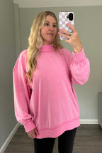 Pink mockneck sweatshirt worn with black leggings, showing its oversized fit and ribbed cuffs